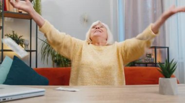 Başarıyı kutlayan, kazanan, hedefe ulaşan, maaş, gelir, emekli maaşı, ev içinde piyango şansı. Yaşlı olgun büyükanne masada oturuyor.