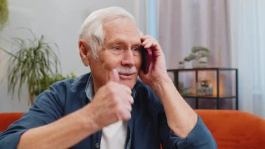 Telefon, iyi haber, dedikodu. Akıllı telefondan hoş sohbetler yapan mutlu, yaşlı bir adam evde arkadaşıyla konuşmaktan zevk alıyor. Yaşlı, olgun büyükbaba masada koltukta oturuyor.
