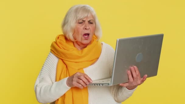 不満のシニアの女性は ノートパソコンのノートブックのタイピング ワーキングの損失宝くじの悪い結果によって驚かれるようになります 幸運はゲームの失敗コンピュータ ウイルスを失いました 黄色の背景にある高齢のおばあちゃん — ストック動画