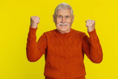 Başarılı zaferi, kazananı, doğum gününü, piyango ikramiyesini, gol atmayı, iyi haberleri, zaferi kutlayan mutlu kıdemli adam. Yaşlı büyükbaba sarı arka planda izole edilmiş.