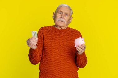 Zavallı yaşlı adam yetersiz miktarda para, kumbarası ve bir dolar banknotu var. Finansal kriz. İflas. Yoksulluk ve yoksulluk. Sarı arka planda olgun büyükbaba emeklisi