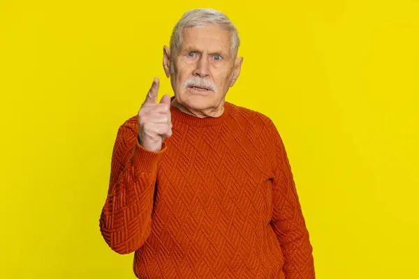 Quarrel. Displeased aggressive unhappy senior old man gesturing hands with irritation and displeasure, blaming scolding for failure, asking why this happened. Mature grandfather on yellow background