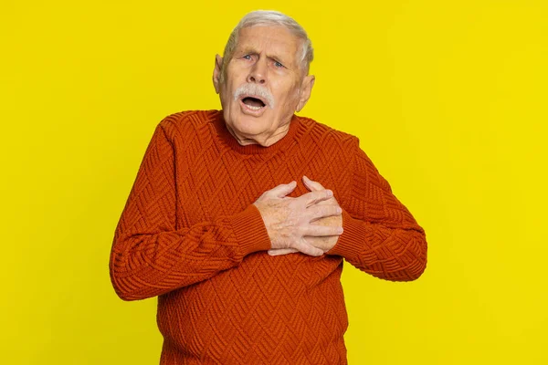 Stressed scared senior man suffers from tension holding chest with heart pain attack risk of stroke pressure symptom, feeling bad sick ill. Elderly mature grandfather isolated on yellow background