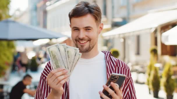 快乐的大胡子男人数着钞票 使用智能手机计算器应用程序 计划在网上预订礼物和食品递送 城市街道上的布鲁内特年轻人游客 — 图库视频影像