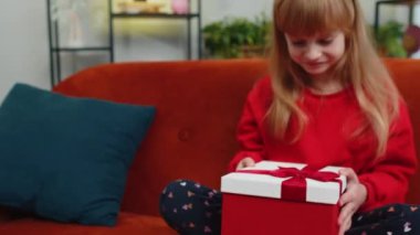 Mutlu küçük kız doğum günü şapkalı şapka hediye paketi takıyor ve kurdele takıyor. Ergen bayan çocuk parti olayını kutluyor, doğum günü hediyesini kanepede açıyor.