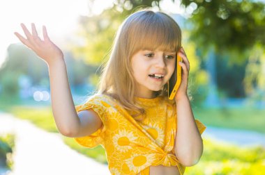 Üzgün, çocukluk çağındaki çocuk, uzaktan iletişim kurarak akıllı telefondan konuşuyor. Sarışın, güzel bir kız. Annesiyle telefonda konuşuyor. Dedikodu yapıyor.