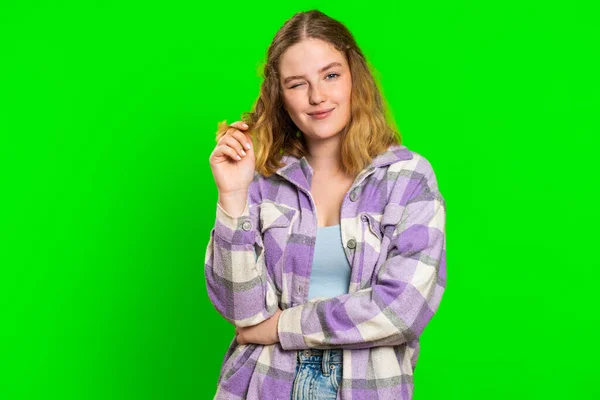 Smiling playful happy young caucasian woman blinking eye, looking at camera with smile, winking, flirting, expressing optimism, good news. Charming redhead girl isolated on green chroma key background