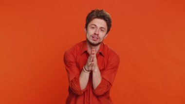 Lütfen, Tanrım yardım et. Beyaz adam kameraya bakarak ve dilek tutarak dua ediyor, umut dolu bir ifadeyle soruyor, özür diliyor, meditasyon yapıyor. Yakışıklı adam turuncu stüdyo geçmişinde izole edilmiş.