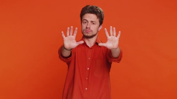 やめろ もう十分だ コーカサス人の男性は 手のひらを折った手を仕上げのジェスチャー 仕上げの警告 アクセスの禁止 コミュニケーションの低下 ボディーランゲージの危険性がないと言います オレンジ色の背景にある若い男 — ストック動画