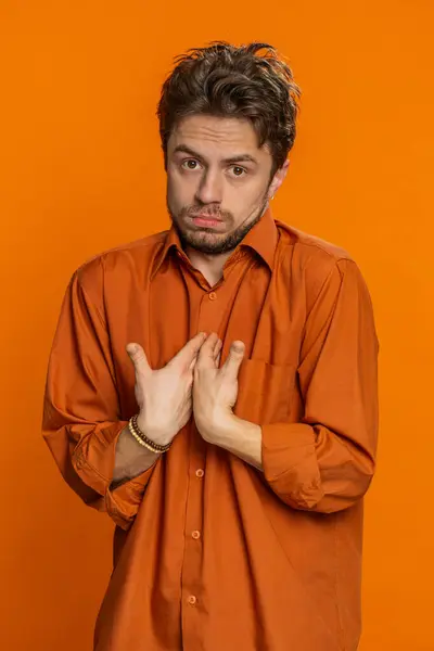 I am not guilty. Confused Caucasian man pointing fingers himself ask say who me no thanks i do not need it feels innocent, not his fault fail. Young guy isolated on orange background indoors. Vertical