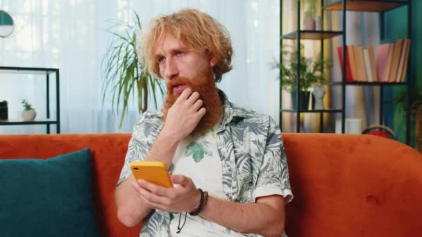 Homem Caucasiano Sentado Sofá Usa Sorrisos Telefone Celular Casa Sala — Vídeo de Stock