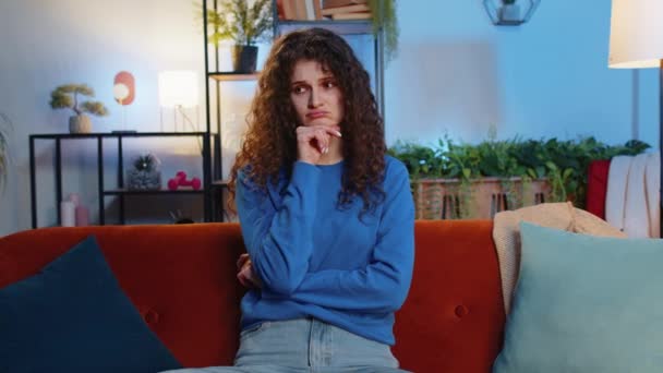 一位穿着休闲装卷发的孤独的年轻女子在家里客厅的沙发上思考着一些问题 厌倦了的女孩在公寓里走神时感到很不舒服 — 图库视频影像
