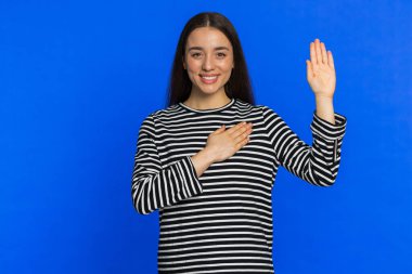 Dürüst olacağıma yemin ederim. İçten, sorumlu, gülümseyen bir kadın yemin etmek için elini kaldırıyor, dürüst olacağına ve doğruyu söyleyeceğine söz veriyor, elini göğsüne koyuyor. Mavi stüdyo arka planında izole edilmiş bir kız. Yaşam Tarzları