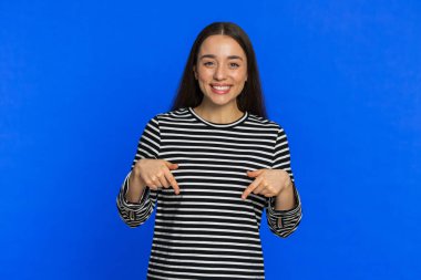 Reklamlara bak. Aşağıdaki genç kadın abone olmak, el kol hareketi yapmak, ticari ve promosyon bilgilerine yer vermek için işaret ediyor. Mavi stüdyo arka planında izole edilmiş güzel bir kız. Kopyalama alanı