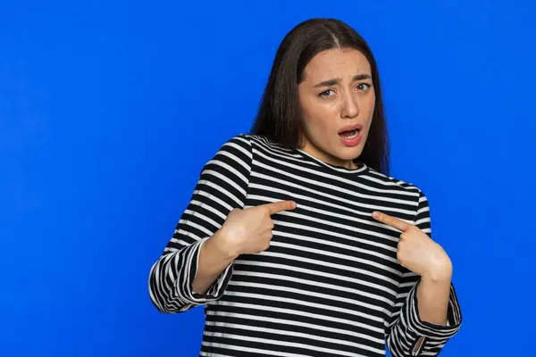 I am not guilty. Caucasian young woman pointing fingers herself ask say who me no thanks i do not need it, feels innocent, not her fault, fail mistake. Girl isolated on blue background. Copy-space
