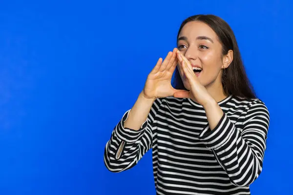 Happy Caucasian young woman yell shout to camera promotion advertisement of holidays sale invitation greetings welcome. Excited smiling girl scream loud isolated on blue background. Copy-space