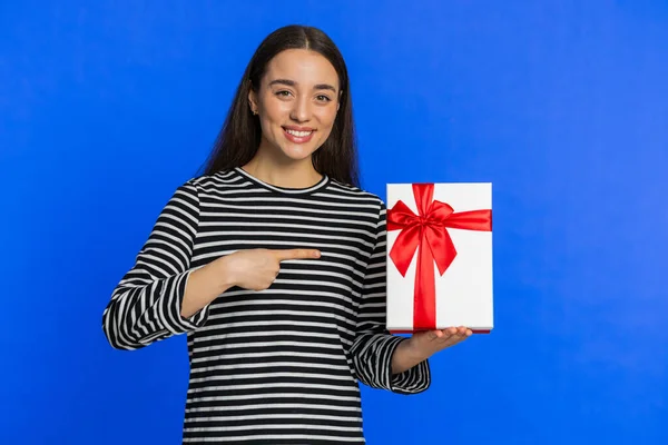 Positive smiling Caucasian woman presenting birthday gift box stretches out hands offer wrapped present career bonus celebrating party promotion discount sale. Pretty girl isolated on blue background