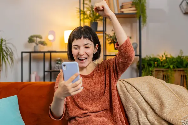 Şaşırmış bir kadın akıllı telefon piyangosuna bakıyor. Oturma odasında kanepede oturuyor. Heyecanlı Kafkasyalı kız dairede zafer kutlaması yapıyor yumruklarını sıkıyor. Mutlu bayan çevrimiçi oyun oynuyor