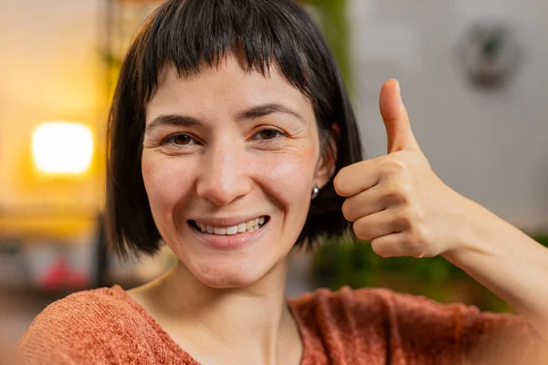 POV of young woman making online video call talking thumb up like gesture looking at camera. Communication, meeting. Smiling Hispanic girl blogger making smartphone conversation at home apartment