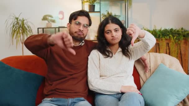 多姿多彩的年轻夫妇的画像 表现出低垂的手势 表达不满 不赞成 不满意 不满的印度家庭看着摄像机坐在客厅的沙发上 — 图库视频影像