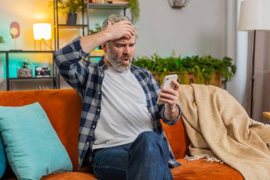 Üzgün, olgun bir adamın elinde akıllı telefonuyla oturup olumsuz mesaj okuması oturma odasında kanepede oturmaktan rahatsız ediyor. Beyaz, yaşlı, yaşlı bir adam dairede alet sorunu yaşıyor. Uygulama çökme konsepti