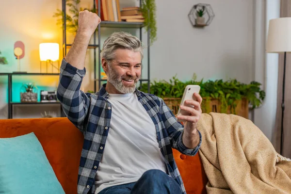 Heyecanlı son sınıf kazananı elinde akıllı telefondan iyi haberler okuyarak online bahis oyununun kazanmasına şaşırdı. Mutlu gri saçlı, beyaz saçlı, yaşlı bir adam. Ekrana bakıyor. Memleketteki zafer başarısından çok memnun..