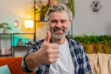 Gibi. Mutlu, heyecanlı, Kafkas kıdemli bir adam kameraya bakıyor ve olumlu haber olumlu geribildirim gösteriyor. Oturma odasındaki koltukta oturan yaşlı sakallı, olgun bir adam..