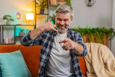 Yaşlı, beyaz sakallı yaşlı adam kamerayı gösterip beni evden aramanı söyledi. Oturma odasında kanepede oturan olgun, gri saçlı yaşlı adam. Ara beni, telefon numaram burada.