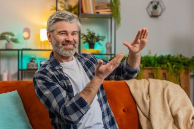 Kendine güveni tam, olgun bir adam harcıyor ya da el hareketleriyle etrafa para saçıyor. Büyük kar getiren vücut dili hakkında daha fazla bahşiş alıyor. Mutlu son sınıf Kafkasyalı orta yaşlı adam dairede koltukta oturuyor.