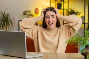 Saldırgan Kafkasyalı genç kadın stres geriliminden bağırıyor panik korku umutsuzluk şaşkınlık şaşkınlık jestler öfke ve gerginlik ifade eder. Öfkeli yetişkin kız evdeki masada oturuyor.