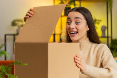 Ofis odasında oturan mutlu beyaz kadın teslimat paketini açıyor. Gülümseyen mutlu kız alışverişci çevrimiçi dükkan müşterisi posta yoluyla satın alma hediyesi alan karton kutuyu açıyor