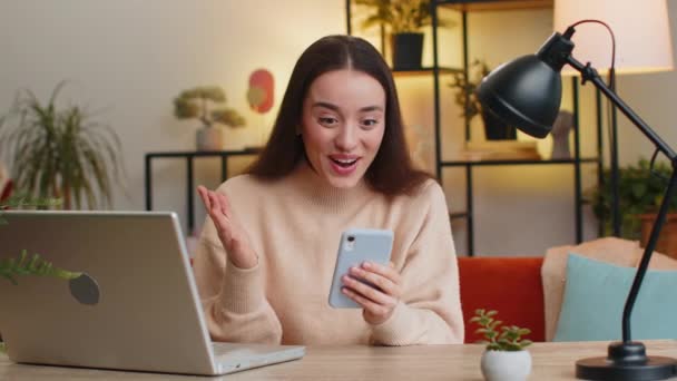 幸せな女性は モバイルスマートフォンタイピングブラウジングを使用しています うわー 成功を祝う勝利宝くじジャックポットの目標達成ゲーム良い肯定的なニュースの勝利 自宅のオフィステーブルにいる少女 — ストック動画