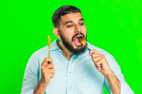 Ready to eat. Hungry Indian man waiting for serving dinner dishes with with restlessness holding cutlery fork knife, will appreciate delicious restaurant meal. Guy isolated on chroma key background