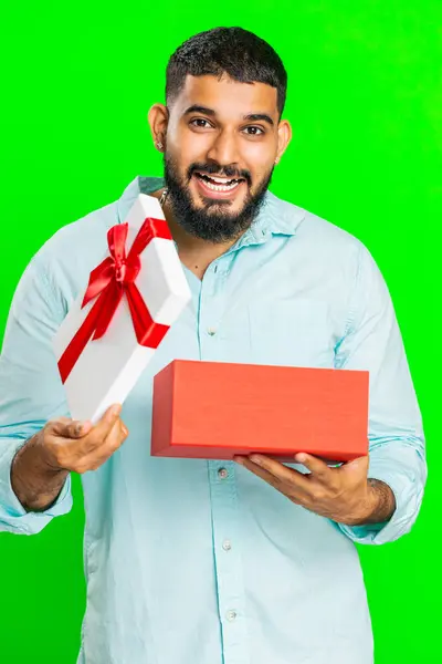 Happy Indian man opening birthday gift box with red ribbon. Holidays surprise concept. Smiling Arabian bearded guy receive great wrapped present celebrating isolated on green chroma key background