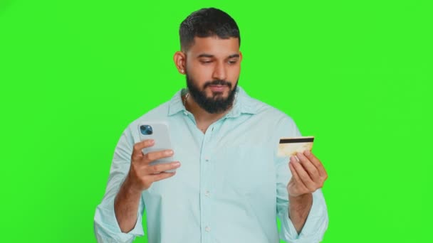 快乐的印度年轻人一边用信用卡和智能手机转移开销 一边在网上购物 订购食物 用绿色彩色键背景隔离的阿拉伯男人 — 图库视频影像