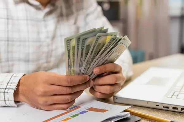 Close-up hands of businessman counting cash money dollar checking salary enjoy richness at modern workplace. Happy freelancer guy calculating currency profit financial savings at home office table.
