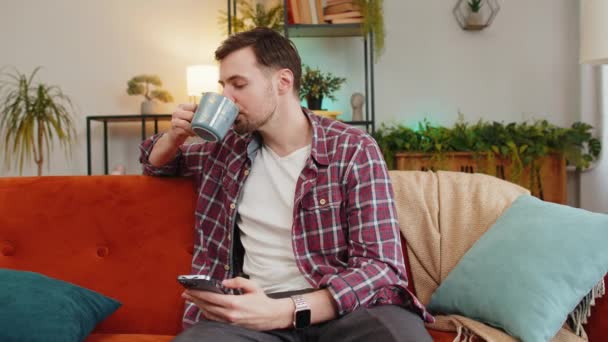 컵에서 뜨거운 커피를 스마트폰을 플레이드 셔츠에 집에서 소파에 친구와 채팅을 — 비디오
