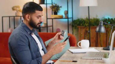 Genç Hintli serbest çalışan kredi kartı ve akıllı telefon kullanarak para transferi yapıyor. Merkez ofisteki masada online alışveriş yapıyor. Uzaktan kumanda işinde çalışan gülümseyen İspanyol adam..