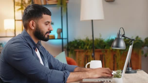 ラップトップでタイプする若いアラビア人のフリーランサーの笑顔 テーブルで自宅から重要なメールを書く男のプロフェッショナル ハッピーヒスパニック男性カジュアルな服でオンライン遠隔仕事をしています — ストック動画