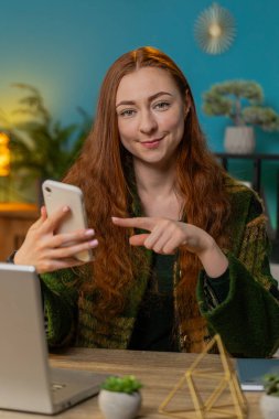 Çevrimiçi akıllı telefon uygulaması kullanarak gülümseyen mutlu kadın ev ofisinden çalışan uzaktan kumandayı işaret ediyor. Serbest çalışan kız iyi bir mobil program kullanmayı öneriyor. Dikey