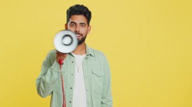 Hintli genç adam megafonla konuşuyor, haberleri duyuruyor, reklam indirimlerini yüksek sesle duyuruyor, konuşma yapmak için hoparlör kullanıyor. Stüdyo sarı arka planda izole edilmiş mutlu Arap adam.