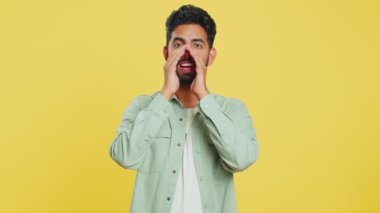 Mutlu Hintli genç adam bağır, kameraya bağır, tatil indirimi reklamını tanıt, davet et, selamla, hoş geldin. Heyecanlı gülümseyen Arap adam sarı arka planda izole bir şekilde çığlık atıyor.