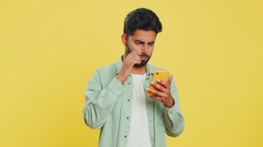 Üzgün Hintli adam akıllı telefon daktilo kullanıyor, oyun oynuyor, kaybediyor, piyango aniden şaşırıyor kötü şans kaybı şanssız haber. Sarı arka planda izole edilmiş Arap Hindu sakallı adam.