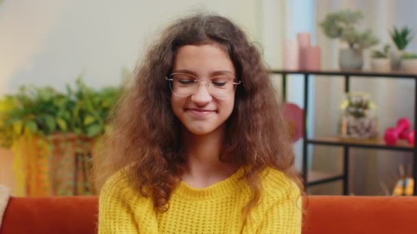 15歳のハッピーな笑顔のコーカサス女子の肖像画 オレンジ色のソファに座っている家の遊びのリビングルームのアパートを見る若い大人の素敵な子供の学生 — ストック動画