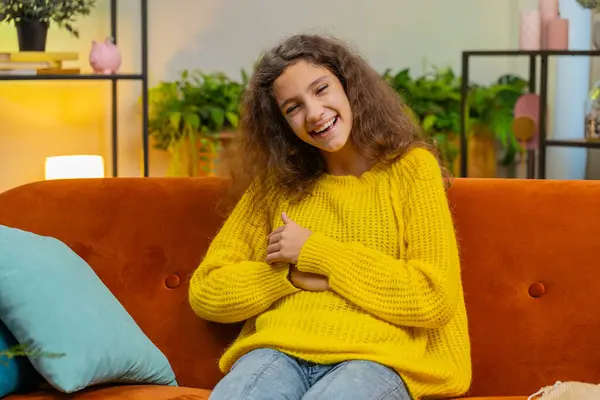 Child girl laughing out loud after hearing ridiculous anecdote, funny joke, feeling carefree amused, positive people lifestyle at home apartment. Teenager female 14-15 years kid in living room on sofa