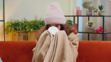 Hasta çocuk, ekoseye sarılı şapka takıyor. Kanepede soğuktan titriyor. Isıtılmamış bir evde sıcak çay içiyor. Sağlıksız çocuk kendini kötü hissediyor, ısınmaya çalışıyor.
