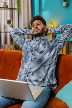 Hintli adam oturma odasındaki işini bitirdikten sonra kanepede oturup dizüstü bilgisayarını kapatıyor. Arap adam serbest çalışıyor. Ev kanepede uzaktan kumandalı çalışıyor. Defter bilgisayarında internete göz atmayı öğrenmek. Dikey