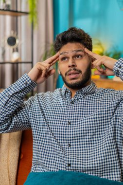 Hasta Hintli adam baş ağrısı problemini tedavi etmek için tapınakları ovuyor, tansiyon, migren, stres, ekşitme, evde yüksek tansiyon. Hintli adam odada kanepede yatıyor. Dikey