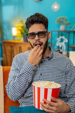 Hintli Hintli adam 3 boyutlu gözlük takıyor, patlamış mısır yiyor TV 'de film içeriği seyrediyor. Gülümseyen İspanyol adam hafta sonları kanepeye oturur ve abur cubur yer. Dikey