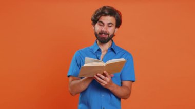 Genç heyecanlı Orta Doğulu adam komik bir masal kitabı okuyor, gülüyor, hobi ediniyor, bilgi sahibi oluyor, eğitim öğreniyor. Arap adam turuncu stüdyoda izole edilmiş.